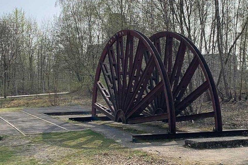 A large metal water wheel structure in a park with trees in the background. 2