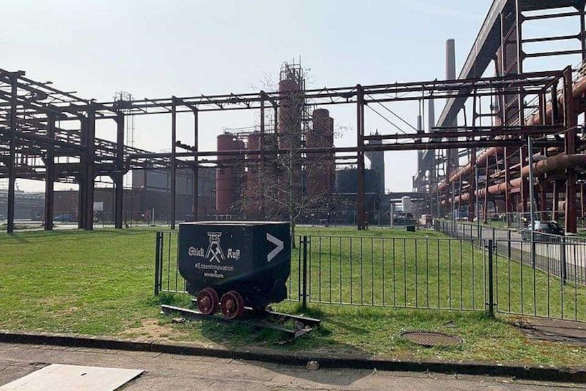 A sign with arrows and text, a grassy area, a metal fence, and industrial structures in the background. 5