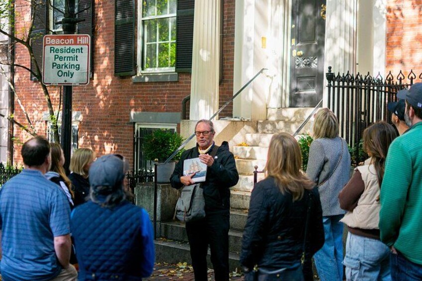 A person speaking to a crowd in front of a building with a 'Resident Permit Parking Only' sign. 4