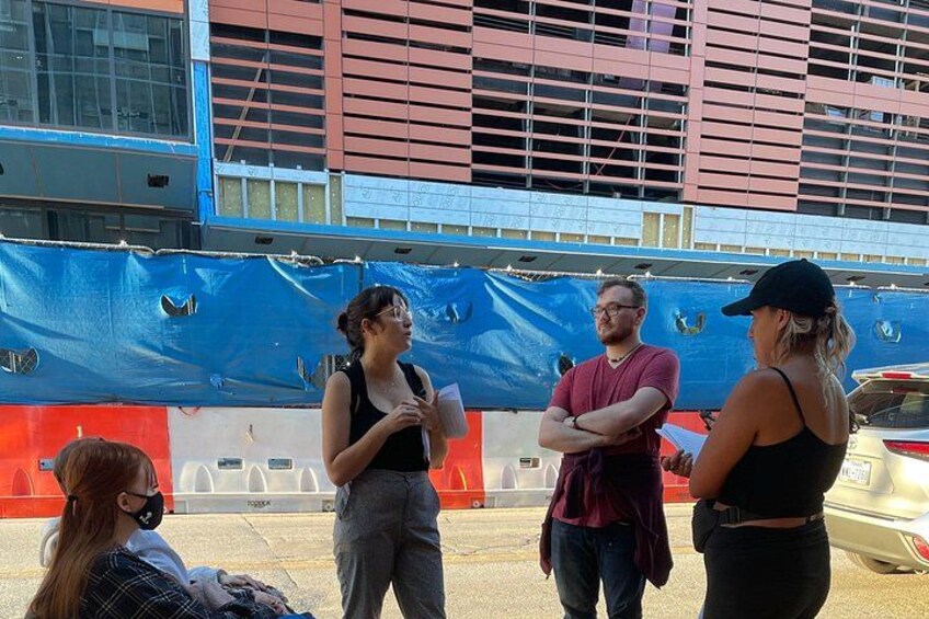 A group of people standing outdoors, a building under construction, and a parked car. 4