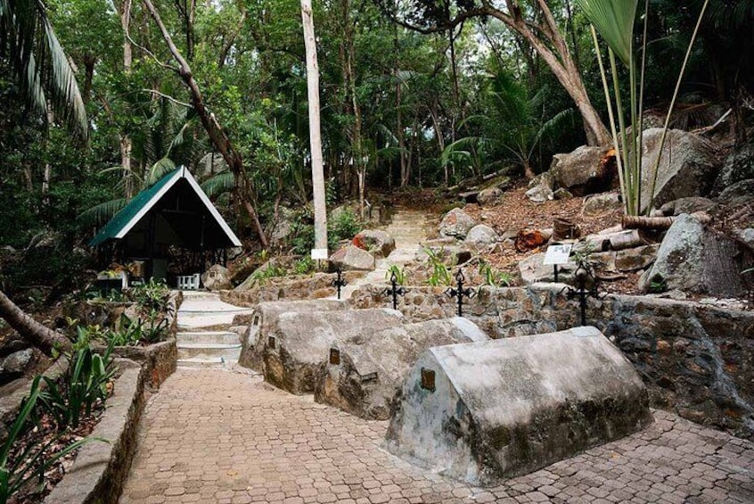 A stone pathway leading to a small shelter in a forested area with large rocks and greenery. 2