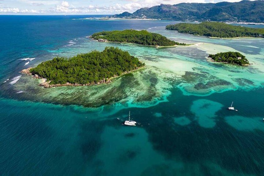 An aerial view of a tropical island with clear turquoise waters, surrounded by lush greenery and distant mountains. 1
