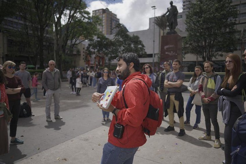 A man in a red jacket holding a sign, standing in a public square with a crowd. 4