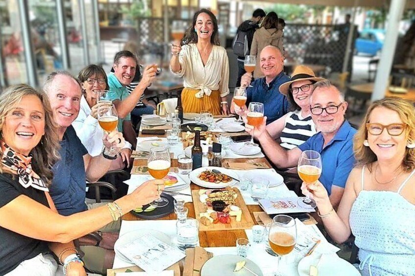 Een groep mensen zit rond een tafel met eten en drinken, in een openlucht omgeving. 3