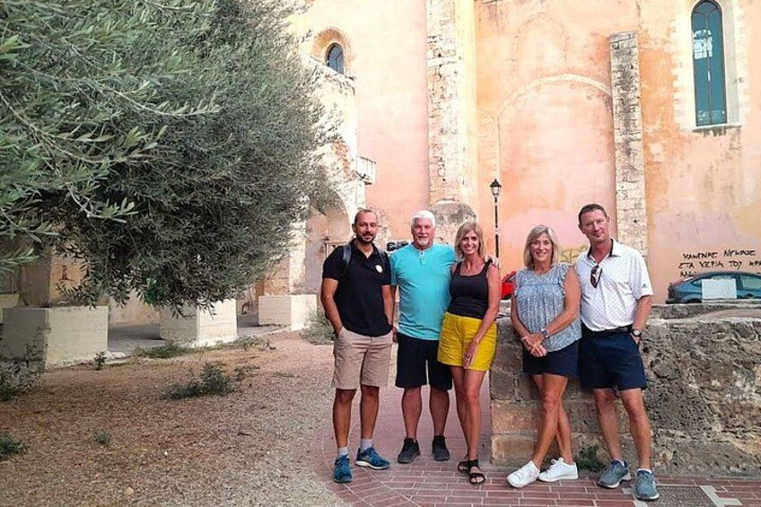 A group of people standing in front of a building with a large tree and a stone wall. 3
