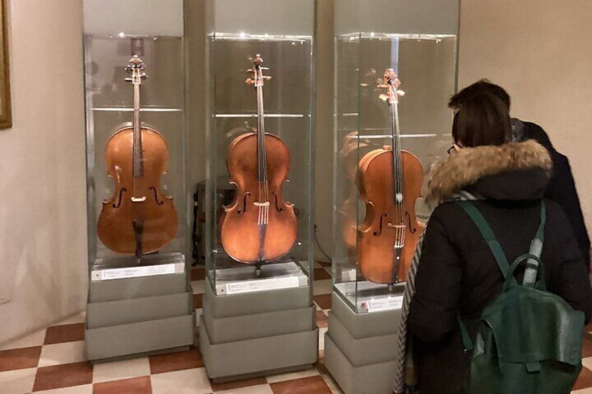 En person betragter tre strengeinstrumenter i glasmontrer. 3