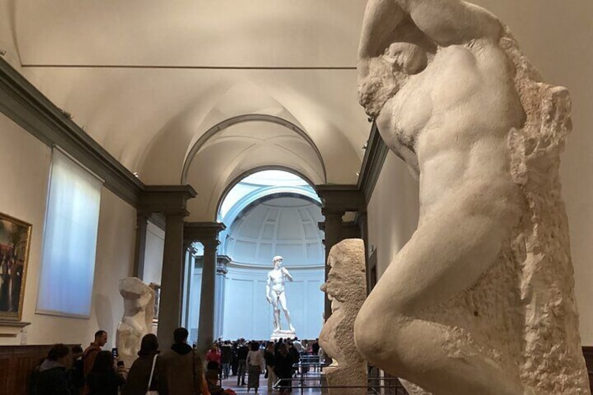 En museums korridor med klassiske skulpturer og en stor statue i baggrunden. 2