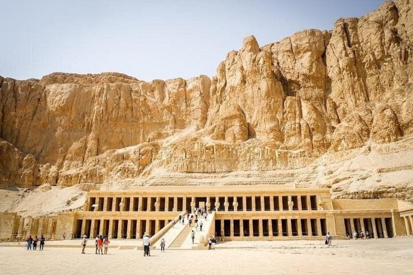 Un gran templo egipcio antiguo con una imponente escalera que conduce a él, ubicado frente a imponentes acantilados de arenisca. 4