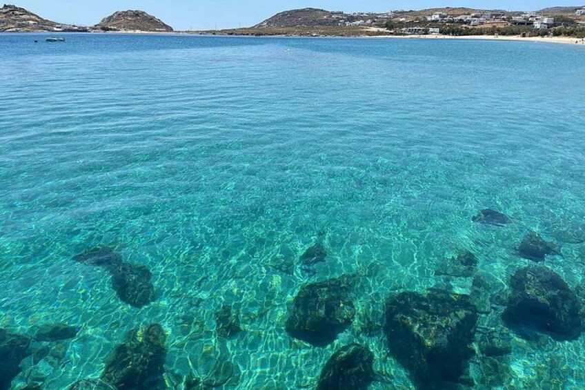 Agua marina turquesa y transparente, formaciones rocosas bajo el agua y una costa distante con edificios. 5