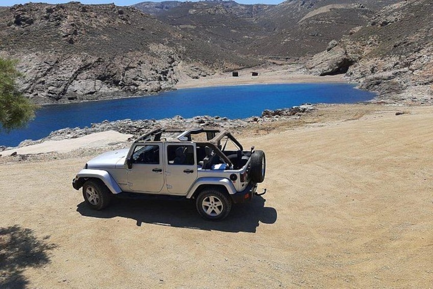 A white off-road vehicle parked on a dirt path near a blue lake surrounded by rocky terrain. 1