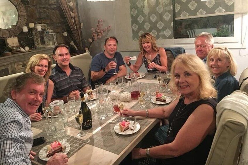 A group of people seated around a table with plates of food, glasses of wine, and a bottle of champagne. 5