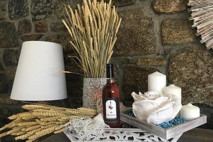 A table with a wine bottle, wheat stalks, candles, and a white lamp against a stone wall backdrop. 2
