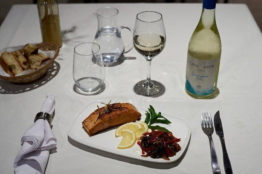 A meal with salmon, lemon, and cranberry sauce on a plate, a bottle of white wine, and a basket of bread on a table. 5