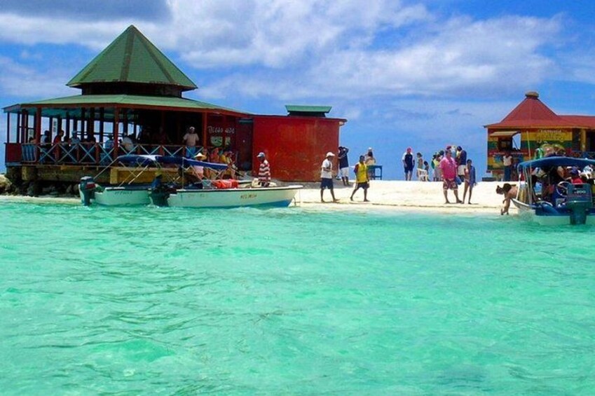 A beach with clear turquoise water, a red building, and a small dock with boats. 4