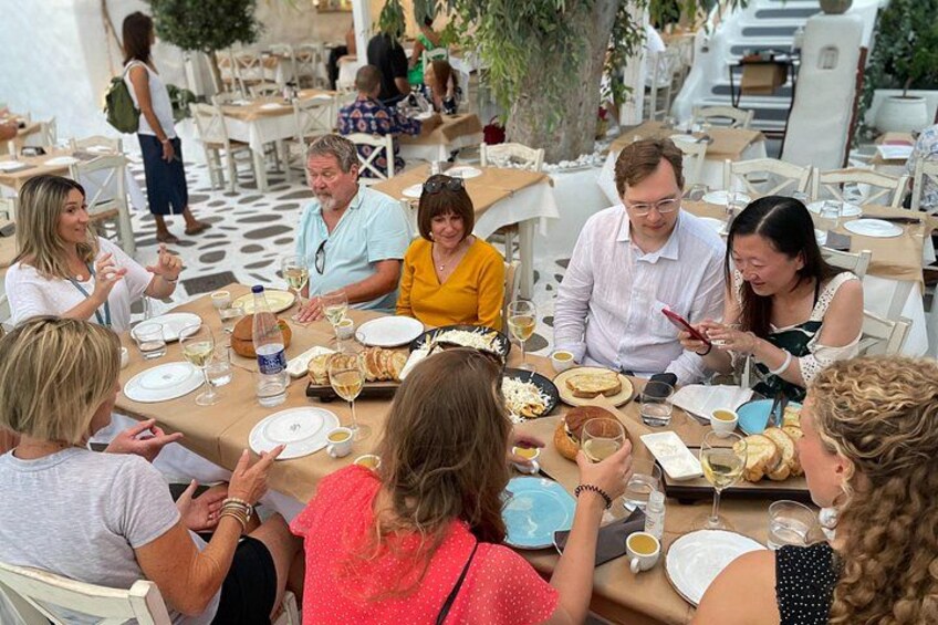 A group of people dining outdoors at a restaurant with white tables and chairs. 4