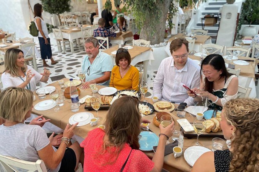 A group of people dining at an outdoor restaurant with tables, chairs, and various dishes. 2