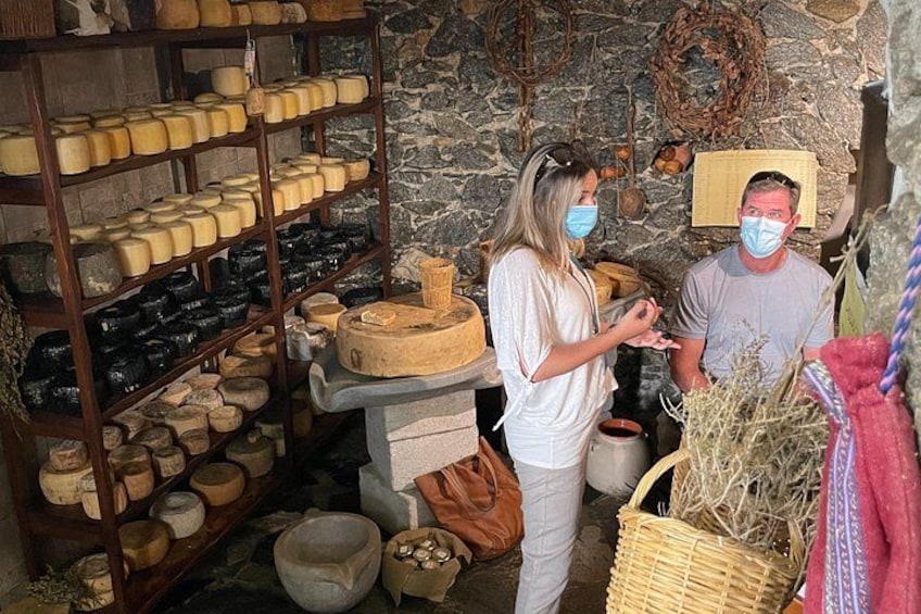 A cheese aging room with shelves of cheese wheels, a stone wall, and a wooden table with cheese molds. 5