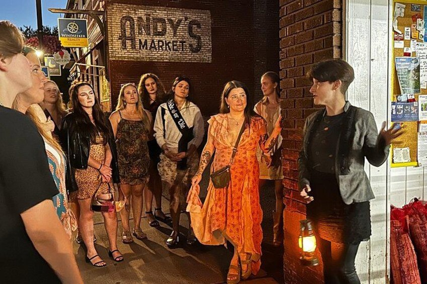 Un grupo de personas de pie frente a un edificio de ladrillo con un letrero que dice 'ANDY'S MARKET'. 3
