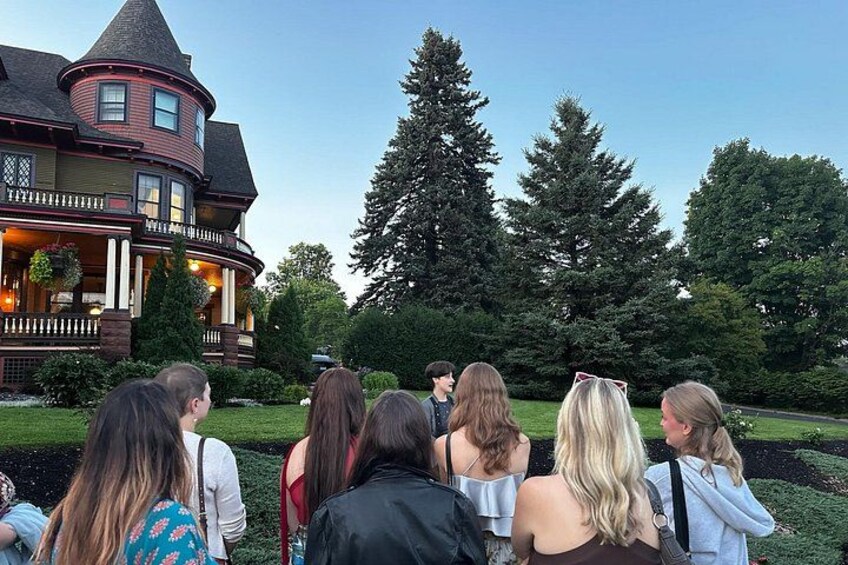 A group of people standing in a garden in front of a large house with a distinctive tower. 5