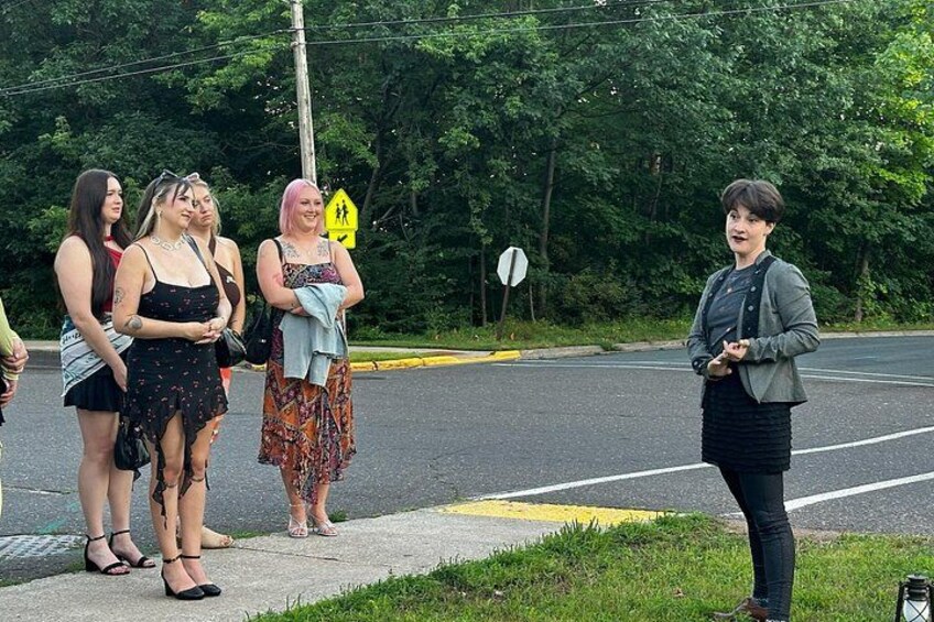 A group of people standing on a sidewalk by a road with trees in the background. 2