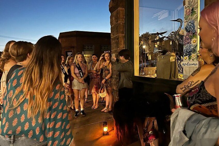 Un grupo de personas de pie en una acera al atardecer, con un edificio y una tienda en el fondo. 2