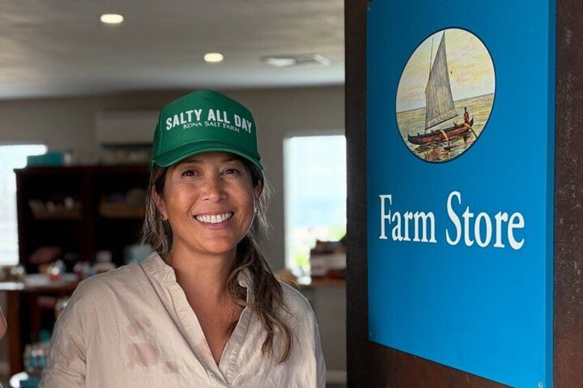 Una persona con gorra verde y texto, de pie frente a un letrero azul que dice "Farm Store" con una ilustración de un velero. 2
