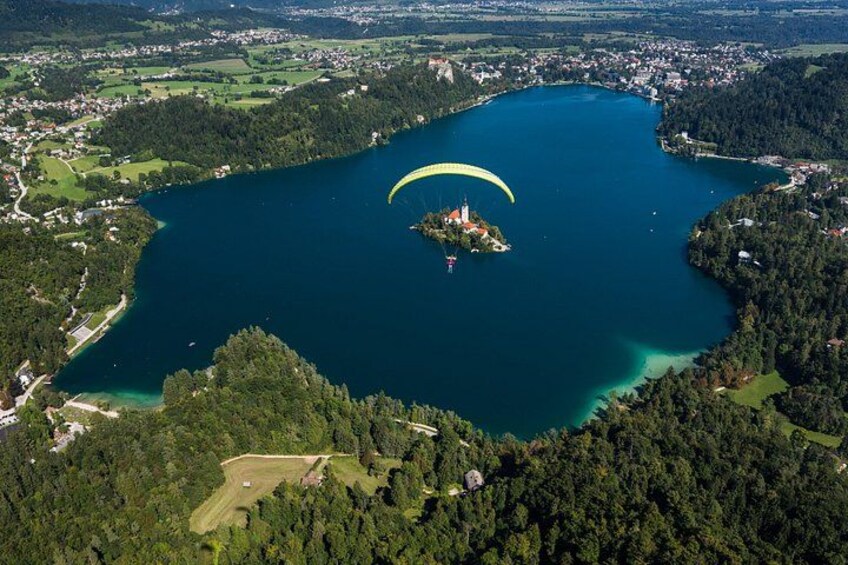 Un lac entouré de forêt, une petite île avec une église, et une personne pratiquant le parapente. 3