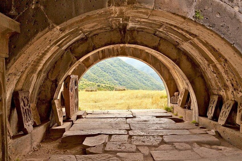 An ancient stone archway leading to a grassy field with a mountain in the background. 4