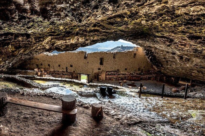 An ancient ruin with a cave entrance, wooden logs, and a snow-covered ground. 3