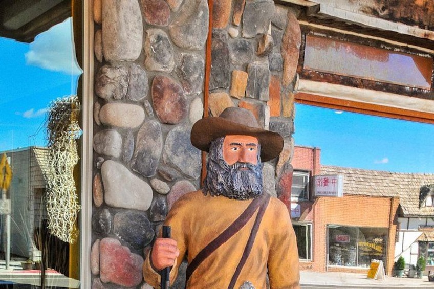 A statue of a man in a hat holding a stick, standing in front of a stone wall with a building in the background. 5