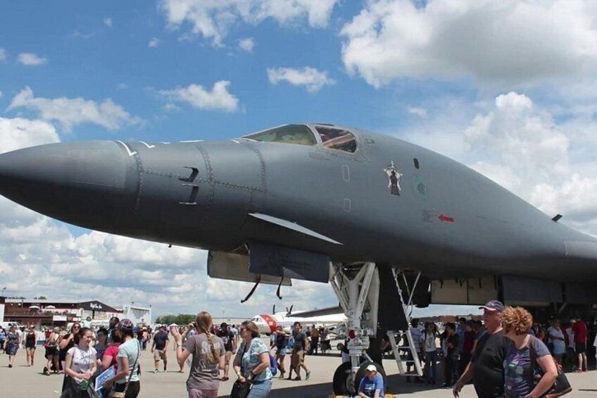 A military jet parked on a tarmac with a crowd of people around it. 4