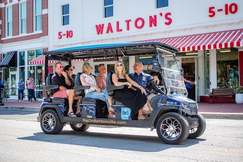 Un carrito de golf con pasajeros frente a una tienda llamada 'WALTON'S'. 1