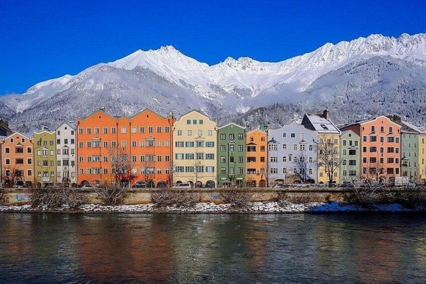 En rad färgglada byggnader längs en flod, med snöklädda berg i bakgrunden. 1