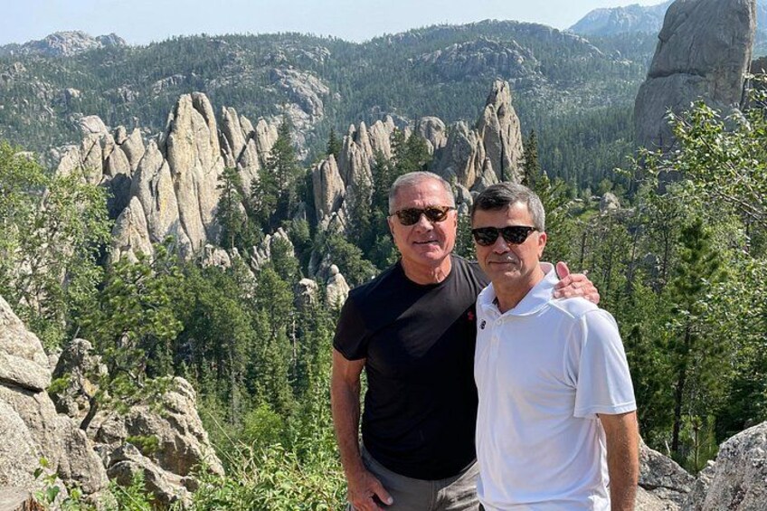 Two people standing on a rocky outcrop with a mountainous landscape in the background. 5