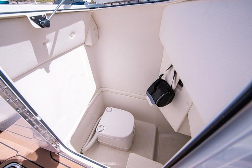 A boat's interior with a toilet, a small storage compartment, and a black container. 5