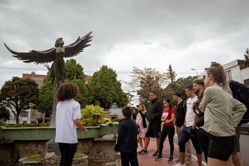 A group of people standing around a statue of a winged figure. 5