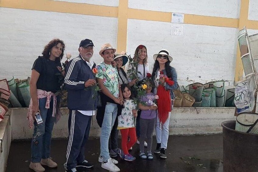 A group of people standing in a room with a white wall and a yellow stripe, holding flowers. 3