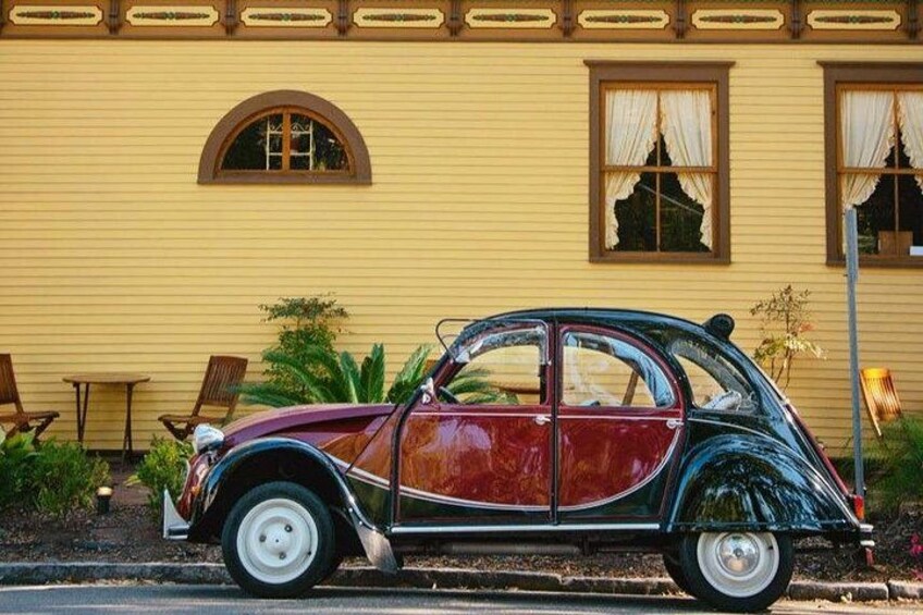 A vintage car parked in front of a yellow house with a garden. 4