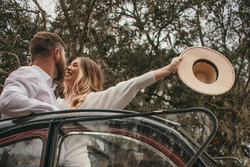 A man and a woman in a convertible car, with trees in the background. 2