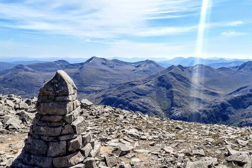 Un montículo de piedras sobre la cima rocosa de una montaña, con vistas a montañas distantes y un cielo despejado. 1