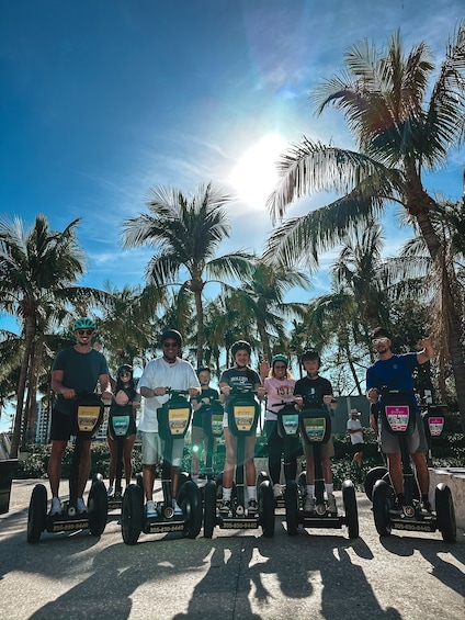 A group of people on Segway scooters in a sunny outdoor setting with palm trees. 2