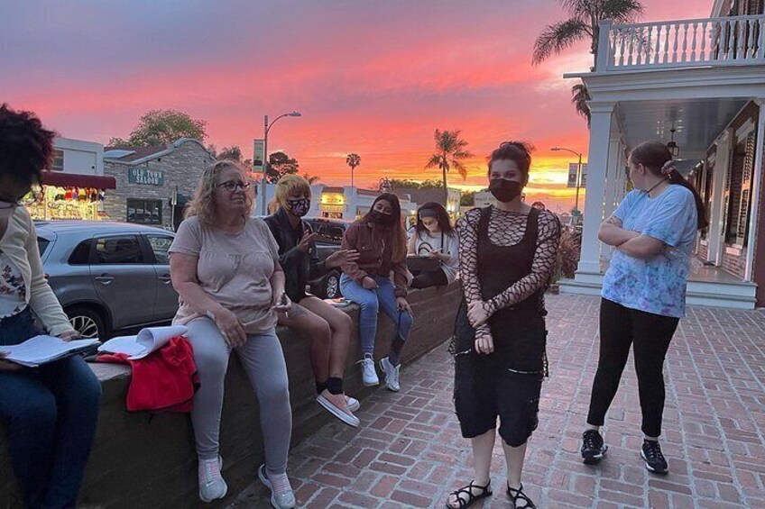 Un grupo de personas sentadas y de pie sobre un pavimento de ladrillo al atardecer. 5