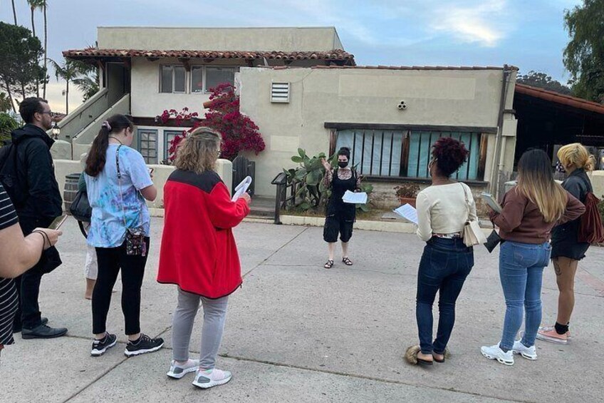 Un grupo de personas de pie al aire libre frente a un edificio con una puerta roja y una escalera. 4