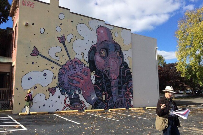 A mural on a building, a parking lot, and a person walking. 1