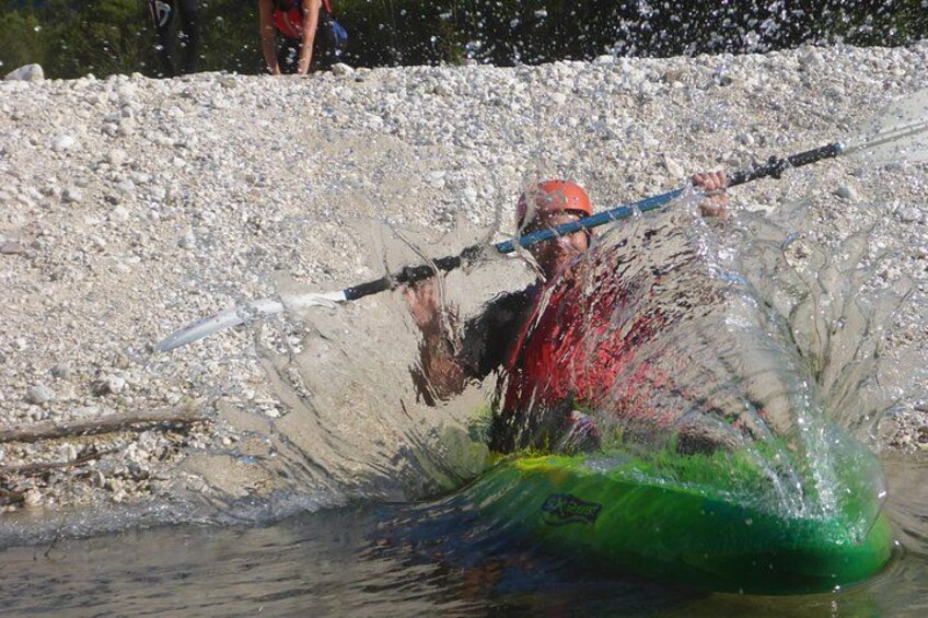 Una persona en kayak surcando el agua, levantando barro, con una orilla rocosa al fondo. 2