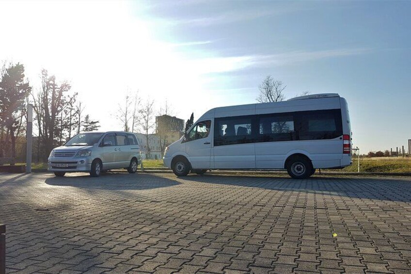 A white van and a silver car parked on a paved area with trees and a clear sky in the background. 5