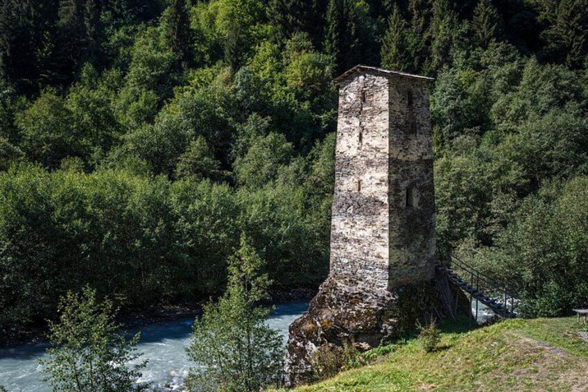 Una torre de piedra junto a un río rodeada de bosque denso. 4