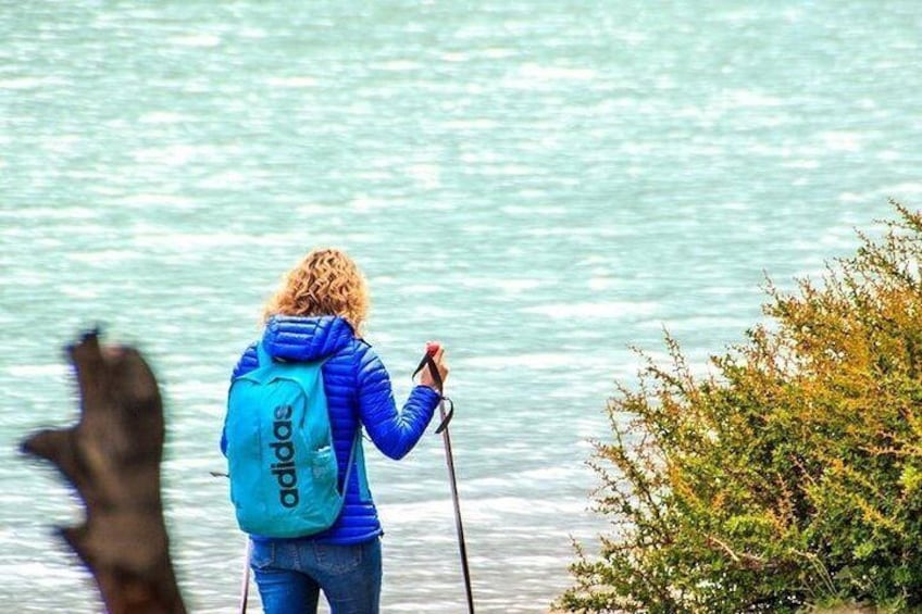 Una persona camina con una mochila azul y un bastón de senderismo cerca de un cuerpo de agua. 1