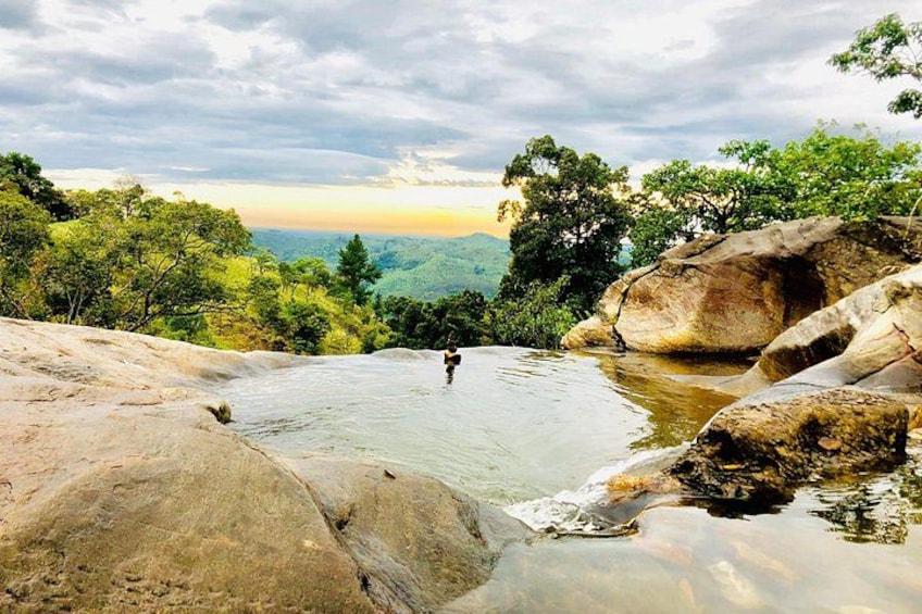 A natural landscape with a person standing in a shallow water body surrounded by large rocks and trees. 3
