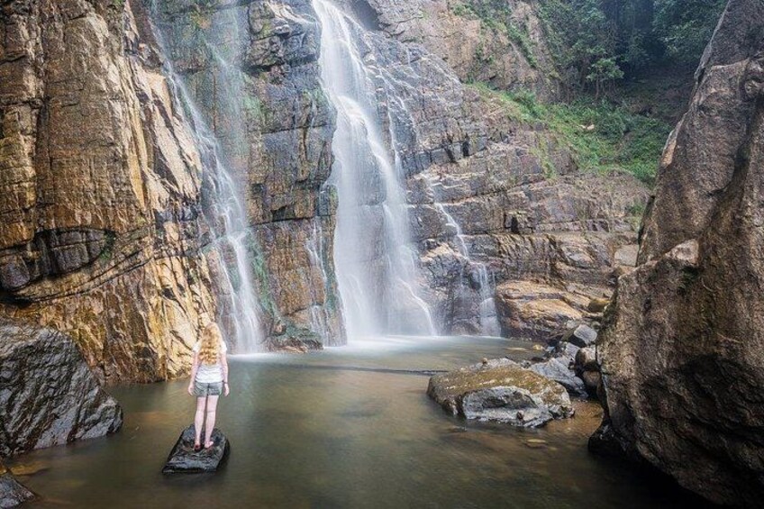 A waterfall in a rocky gorge with a person standing on a rock in the water. 5